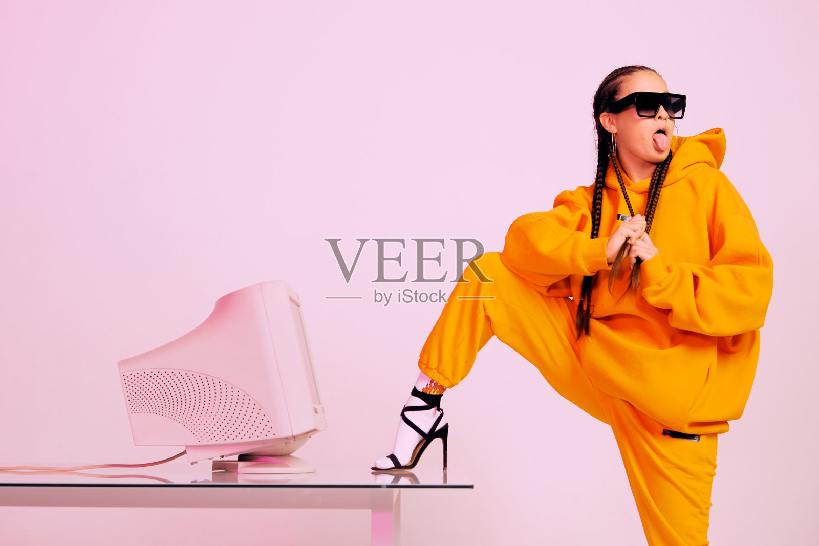 时髦的年轻女办公室职员戴着太阳镜,用老式电脑,脚放在桌子上,露出舌头照片摄影图片