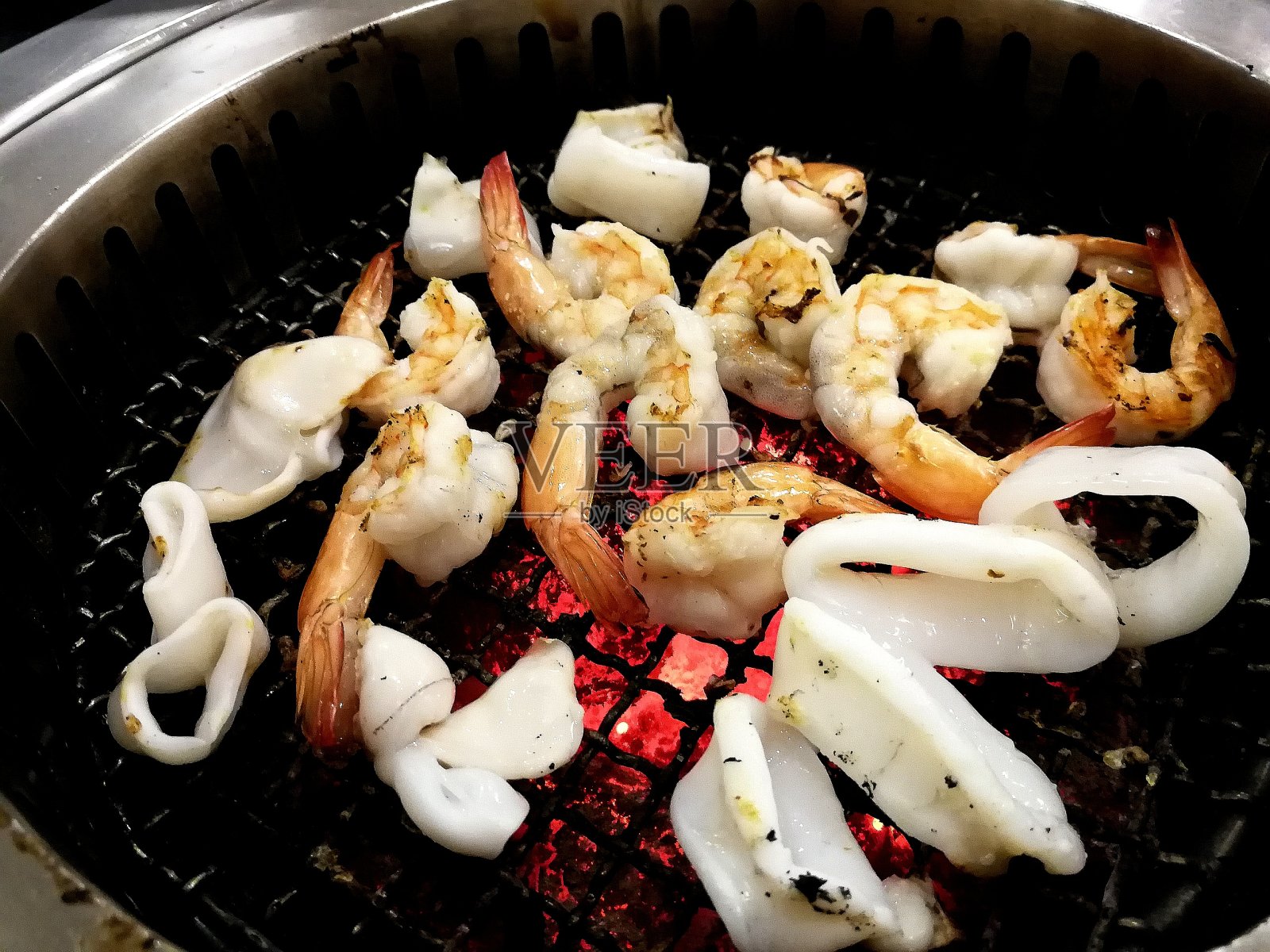 烤虾和鱿鱼在火上,金属格栅。照片摄影图片