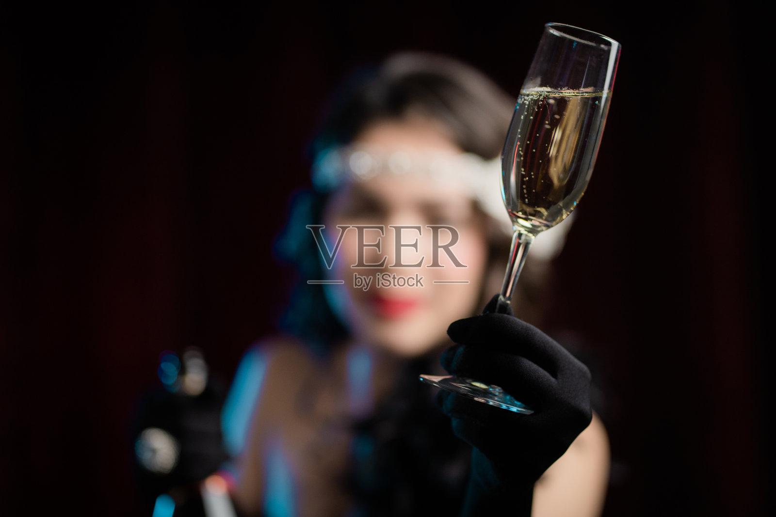 复古风格的女人穿着Flappers的连衣裙举起一杯香槟像吐司,喝葡萄酒在天鹅绒的背景。喧嚣的二十年代,复古,派对,时尚概念照片摄影图片