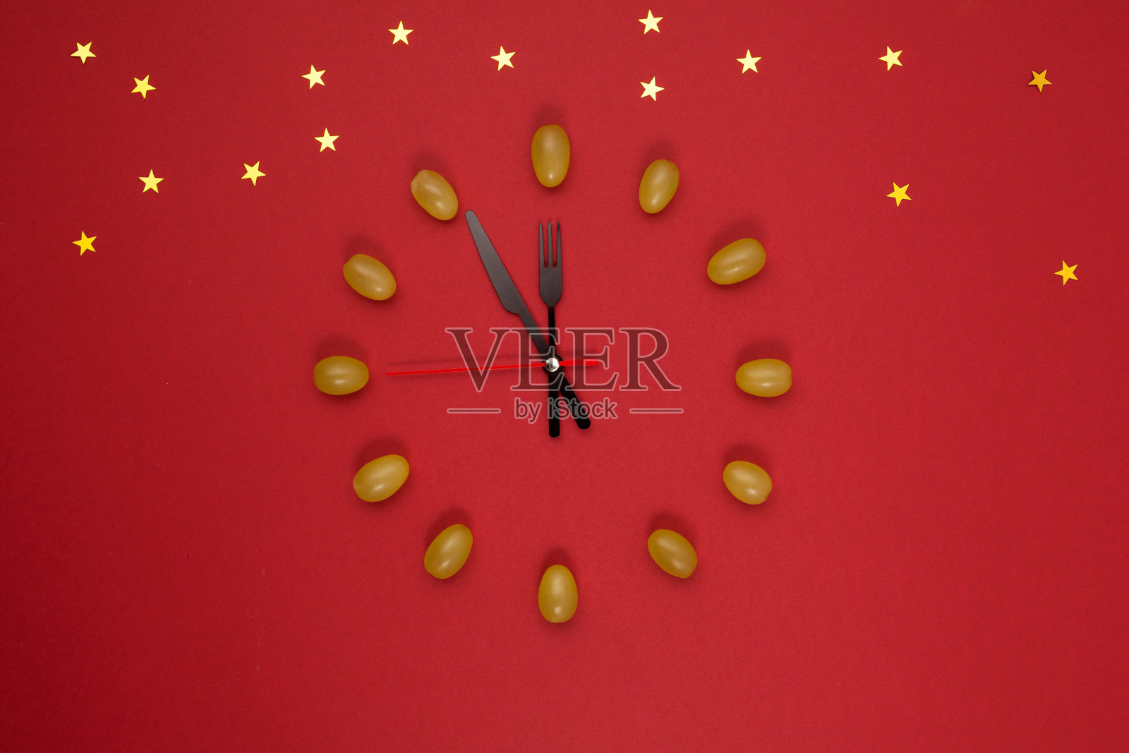 红色背景上12颗葡萄的时钟。圣诞新年作文。有趣的传统是在新年的午夜吃十二颗葡萄以祈求好运照片摄影图片