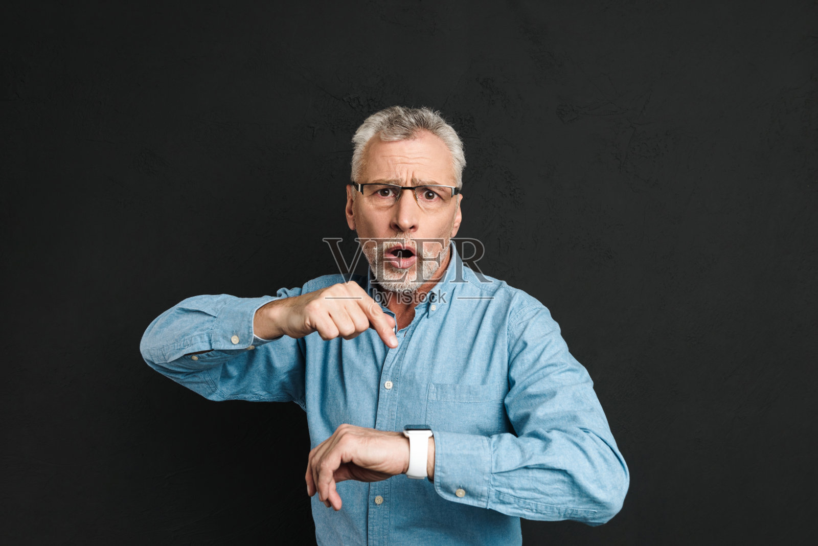 照片紧张的绅士60年代与灰色头发戴眼镜指着他的手表与震惊,孤立在黑色背景照片摄影图片