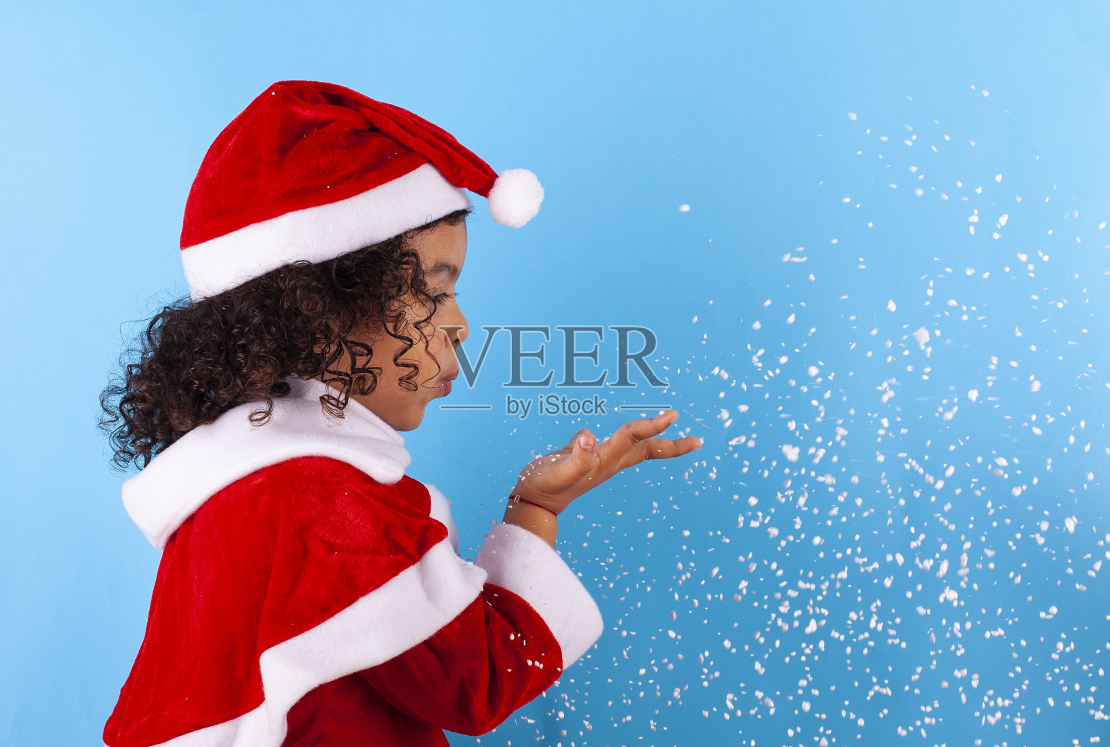 非裔美国小女孩戴着圣诞老人的帽子,吹着雪花照片摄影图片