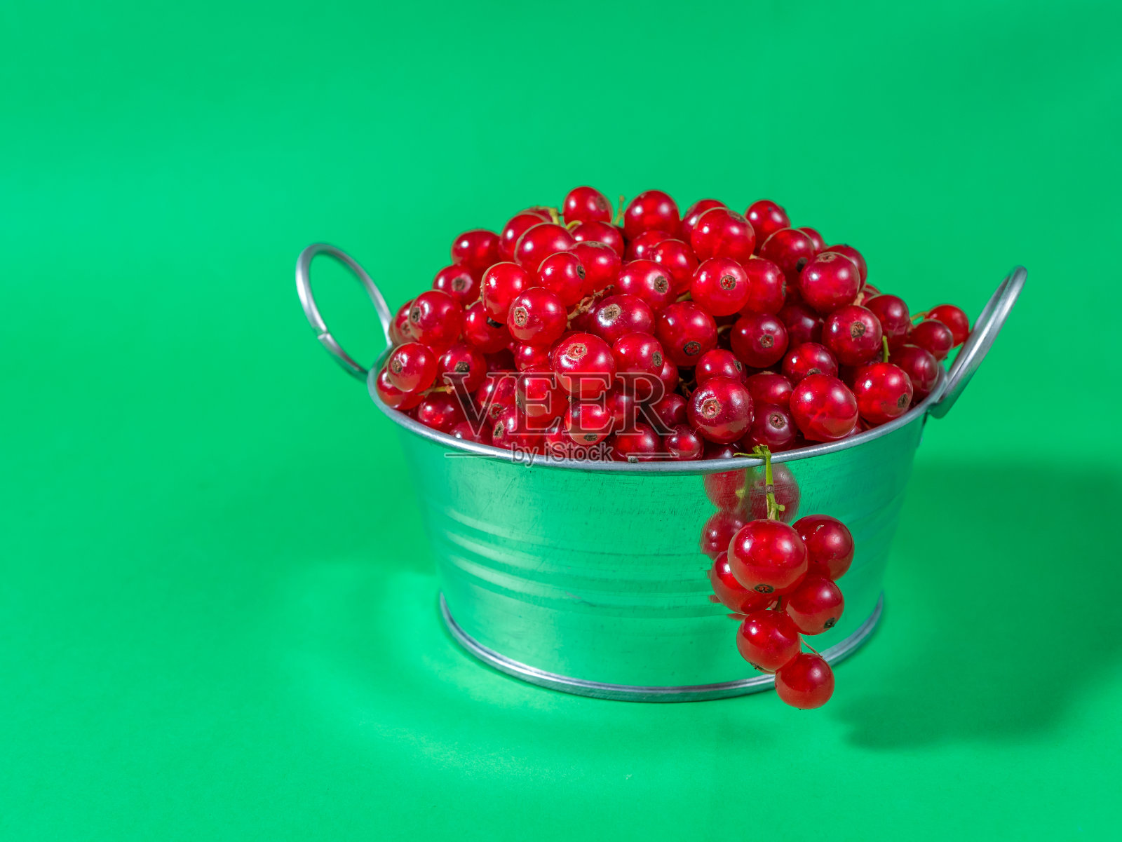 一个装满红醋栗的金属盆,在粉红色的背景上,在绿色的背景上照片摄影图片