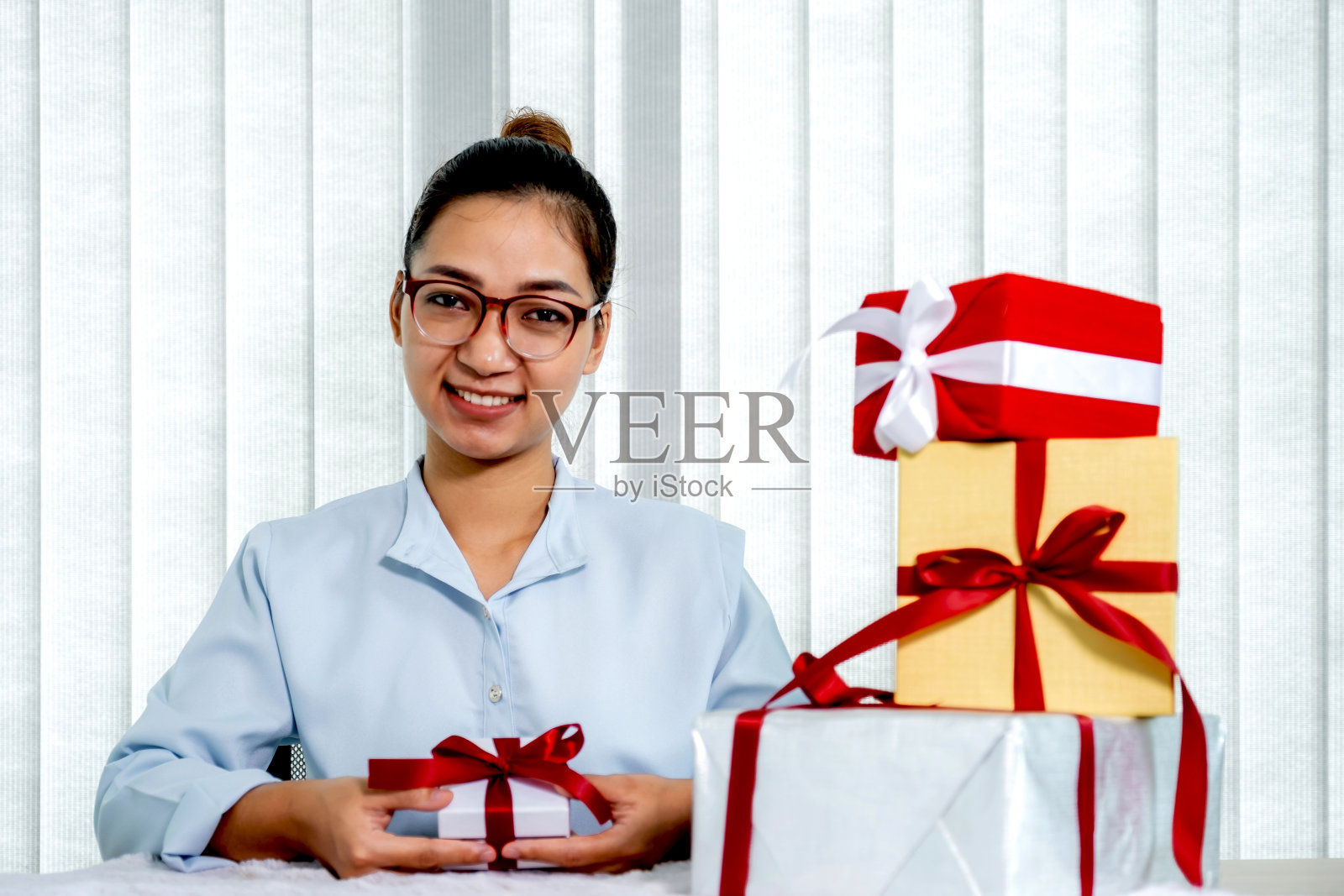 身穿蓝色衬衫的女子拿着一个用红色丝带系着的白色礼盒,礼物是为圣诞节、情人节等特殊节日准备的照片摄影图片