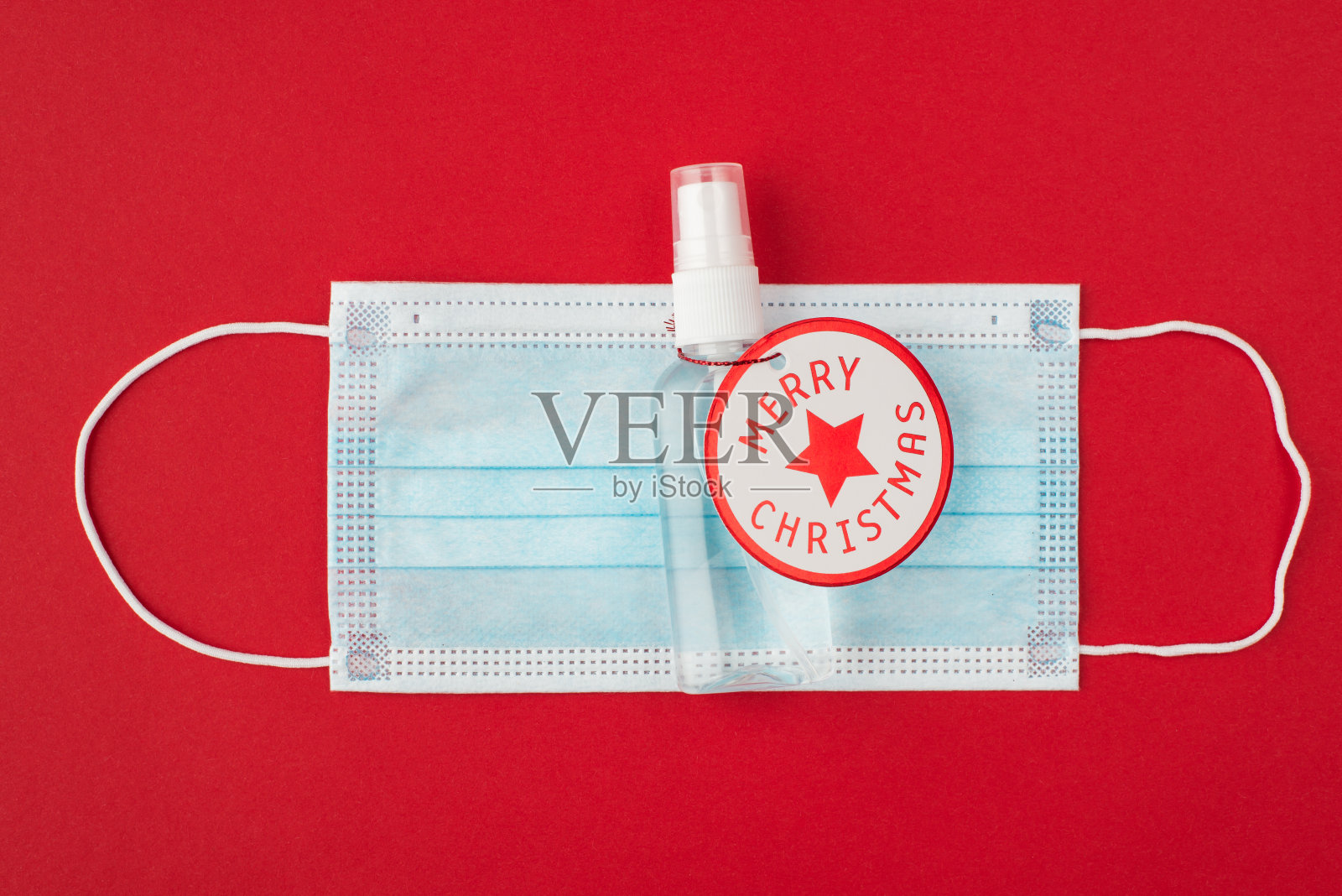 检疫和圣诞节概念,顶部上方俯瞰近距离照片的医疗口罩和手消毒液瓶与圣诞快乐卡片在它孤立的红色背景照片摄影图片