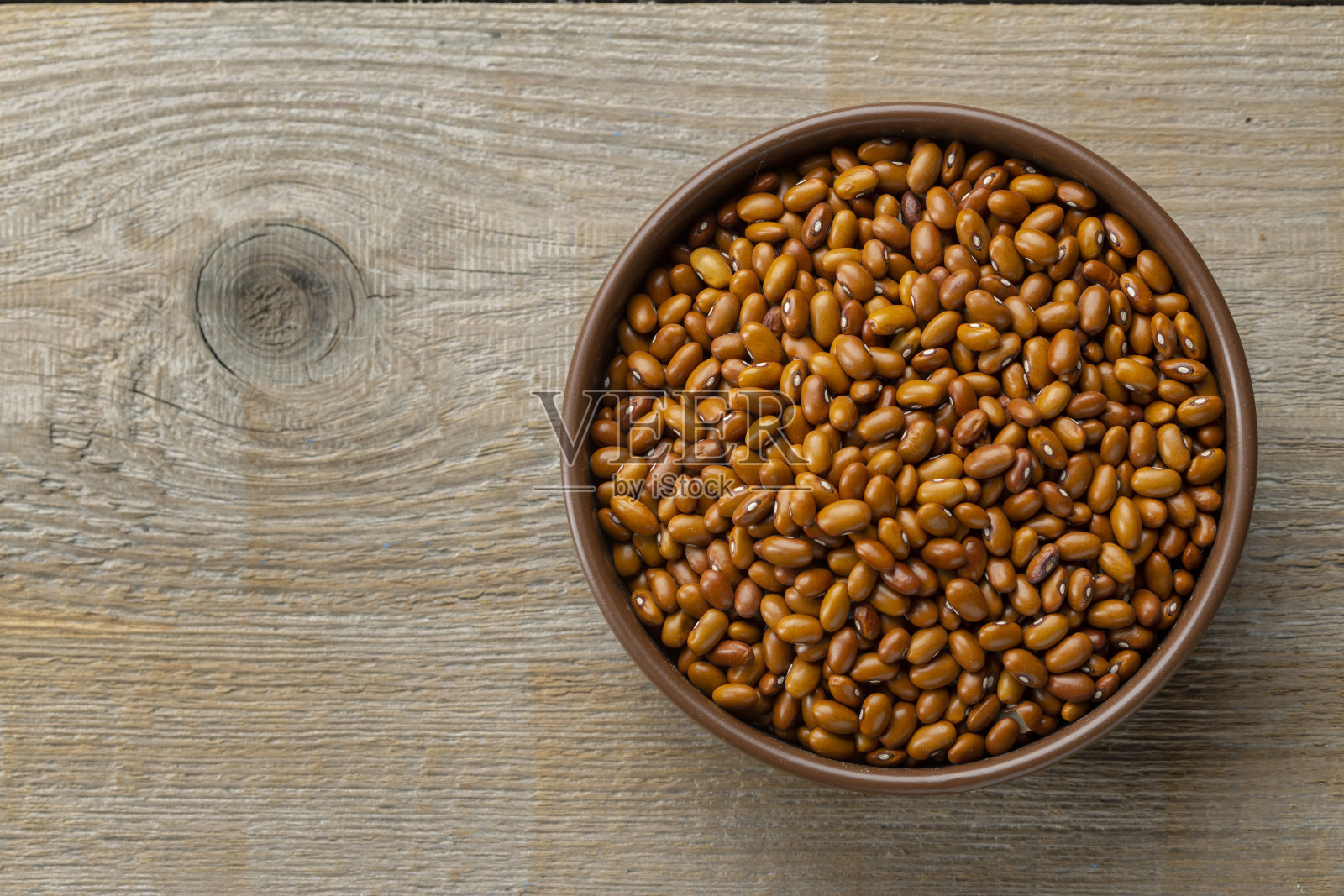 木桌上的陶碗里装着干红豆。空间fot文本。照片摄影图片