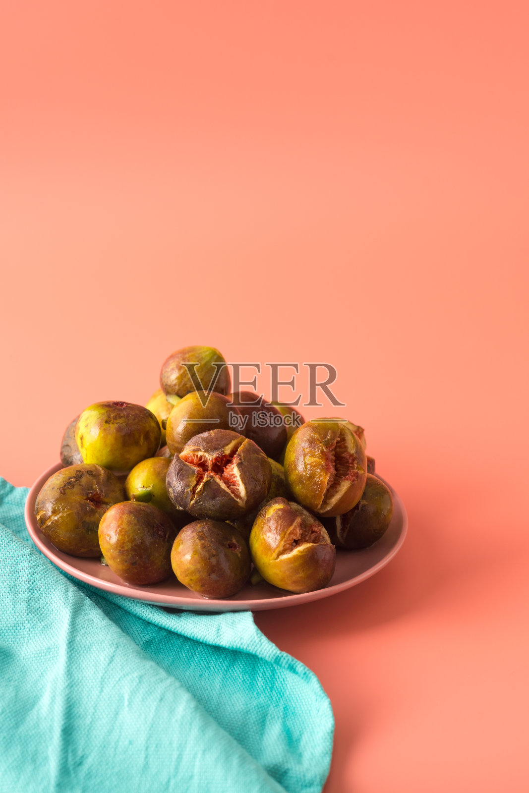许多无花果在粉红色盘子旁边的绿松石亚麻布盘子。垂直的。本空间照片摄影图片