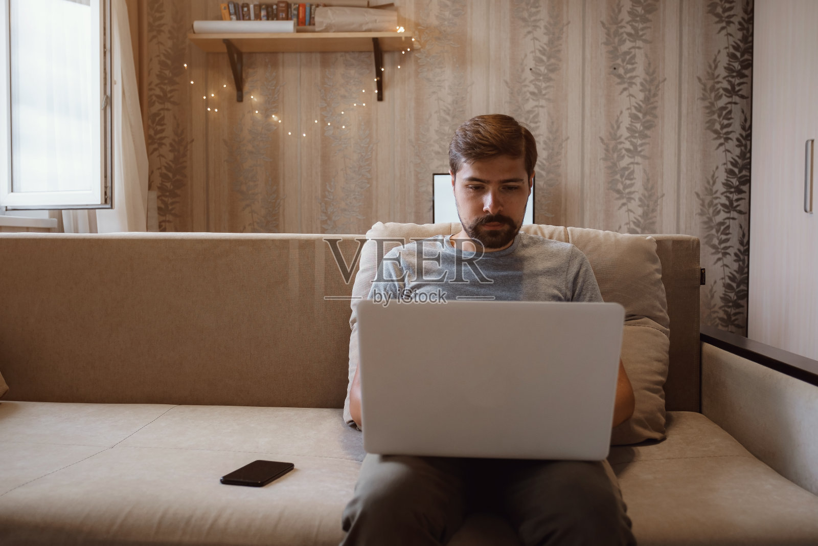 沉思的胡子男子坐在沙发上用笔记本电脑工作照片摄影图片