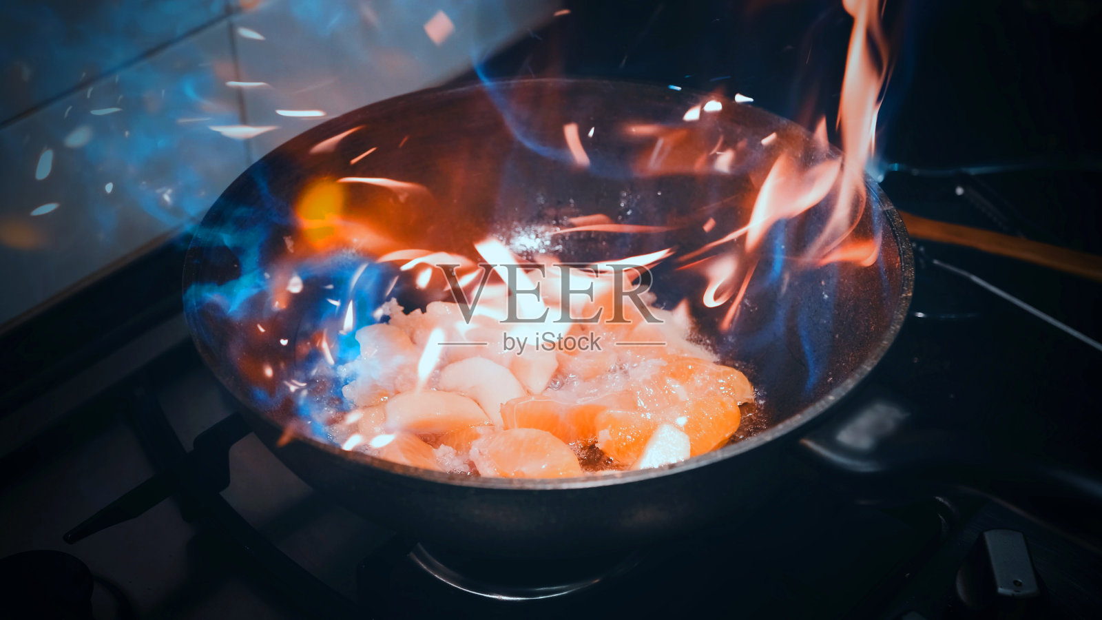 在煎锅里用火煎苹果和桔子。家里的厨房照片摄影图片