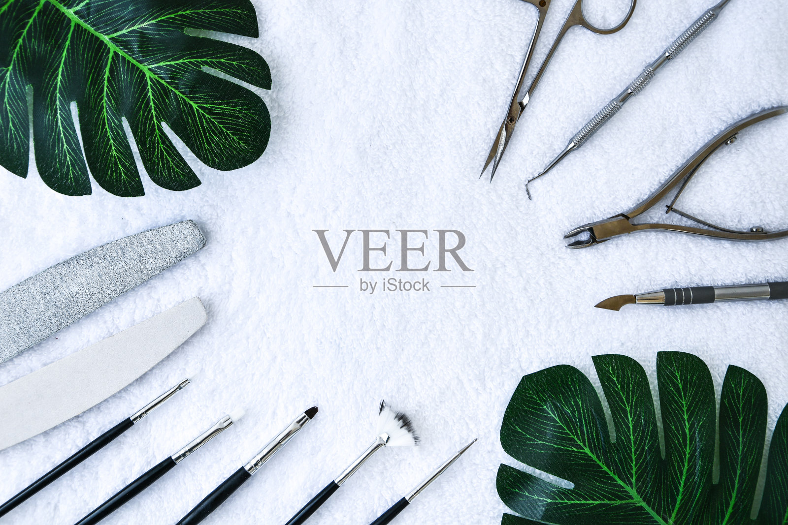 美甲-创造工具,凝胶抛光,所有的指甲治疗,美丽的概念,护理与绿色的叶子在白色毛巾背景。题词沙龙旗帜照片摄影图片