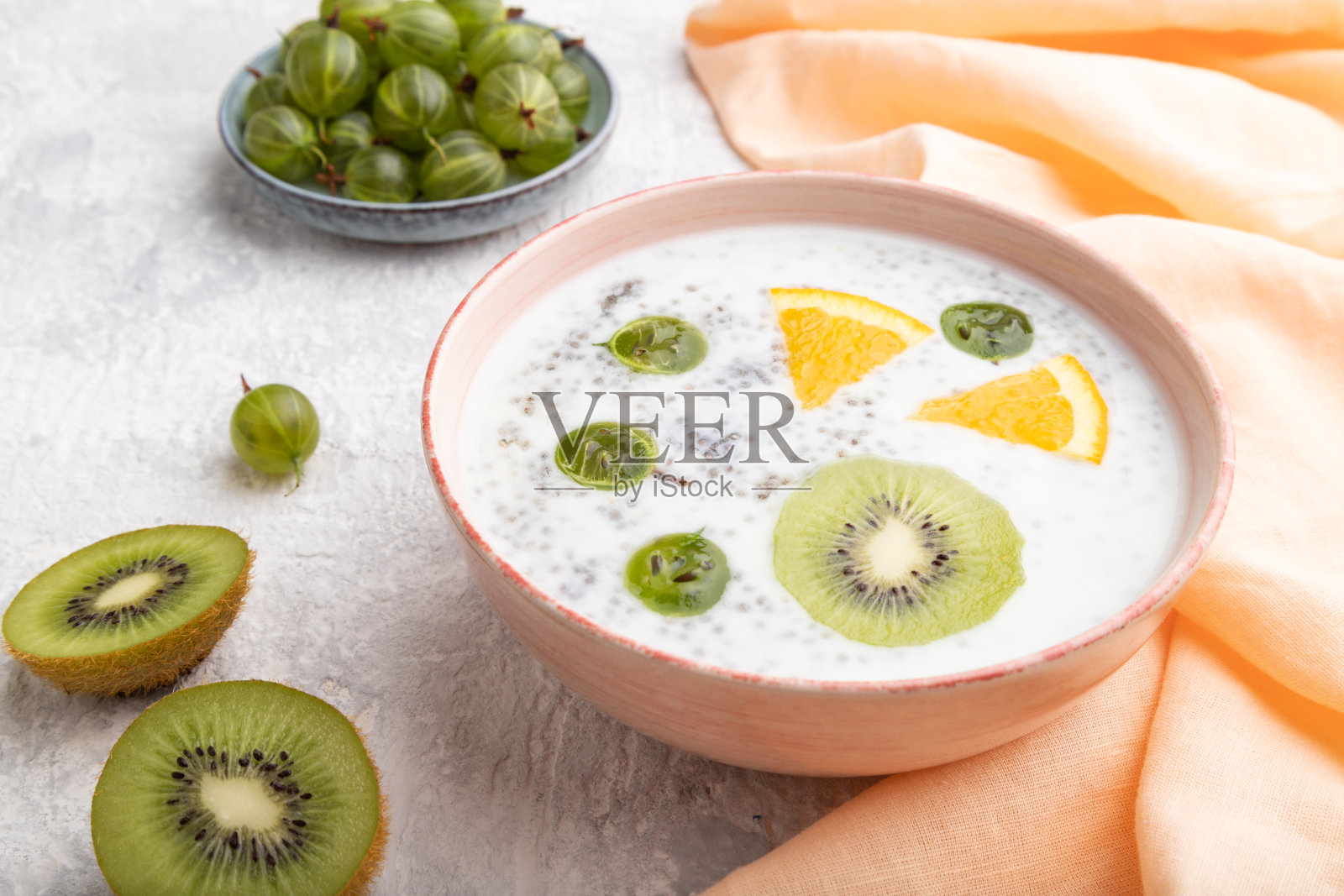 酸奶与猕猴桃,醋栗,嘉在陶瓷碗在灰色混凝土背景和橙色亚麻织物。侧视图,特写。照片摄影图片
