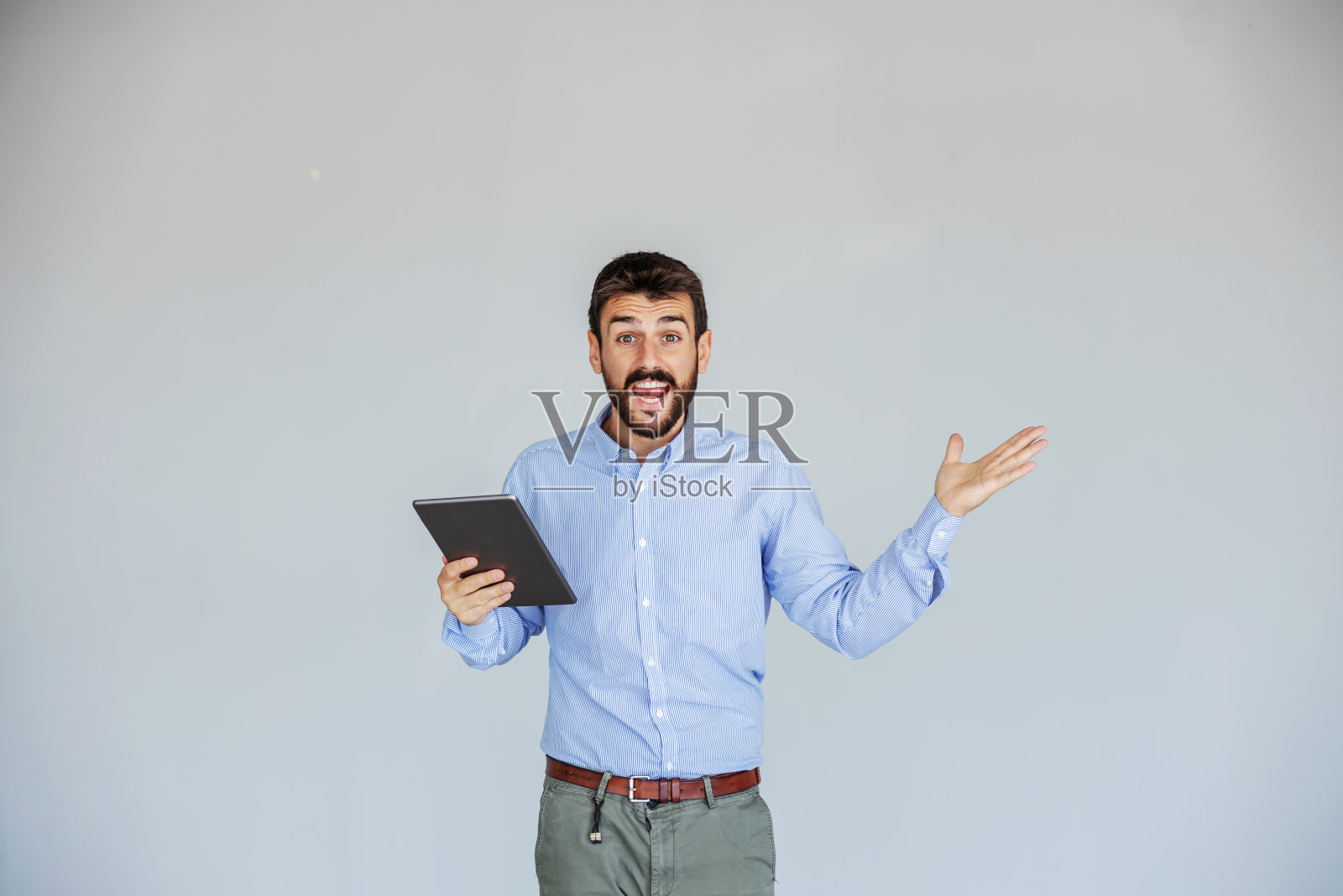 满脸兴奋的大胡子主管站在白墙前,拿着平板电脑看着摄像机。生意做得很好。照片摄影图片