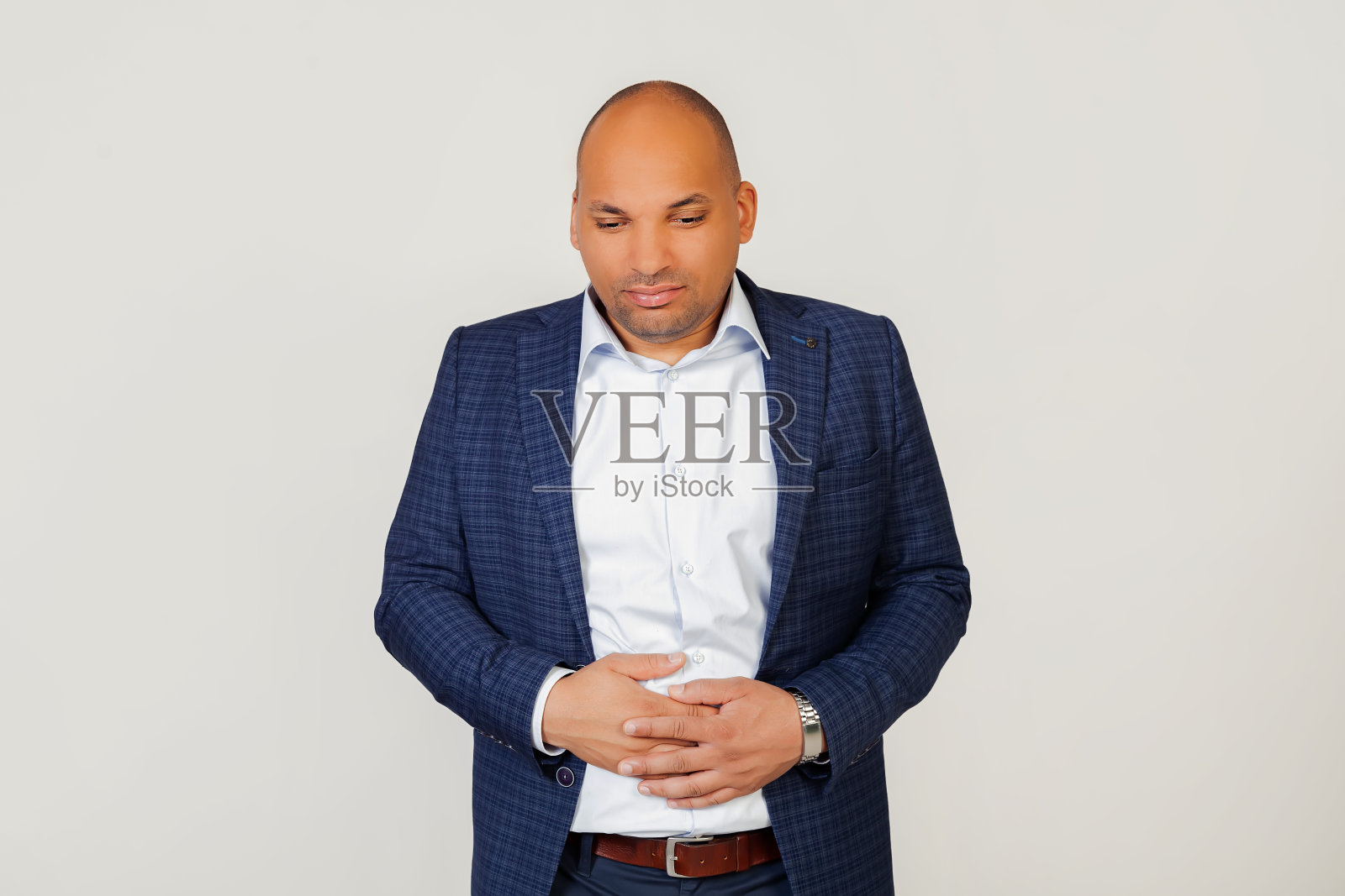 一个生病的年轻非洲裔美国商人的肖像,由于消化不良,一只手放在他的胃上,感觉不舒服。疼痛的概念。站在灰色的背景上。照片摄影图片