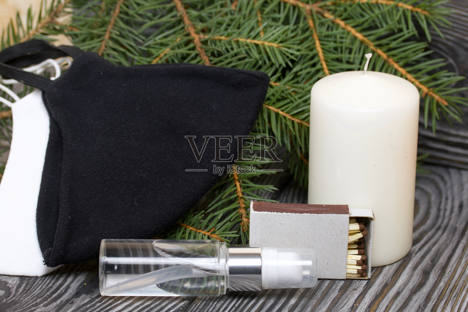 杉树枝和一支蜡烛。附近有医用口罩和杀菌剂。在黑色的松木板上。照片摄影图片