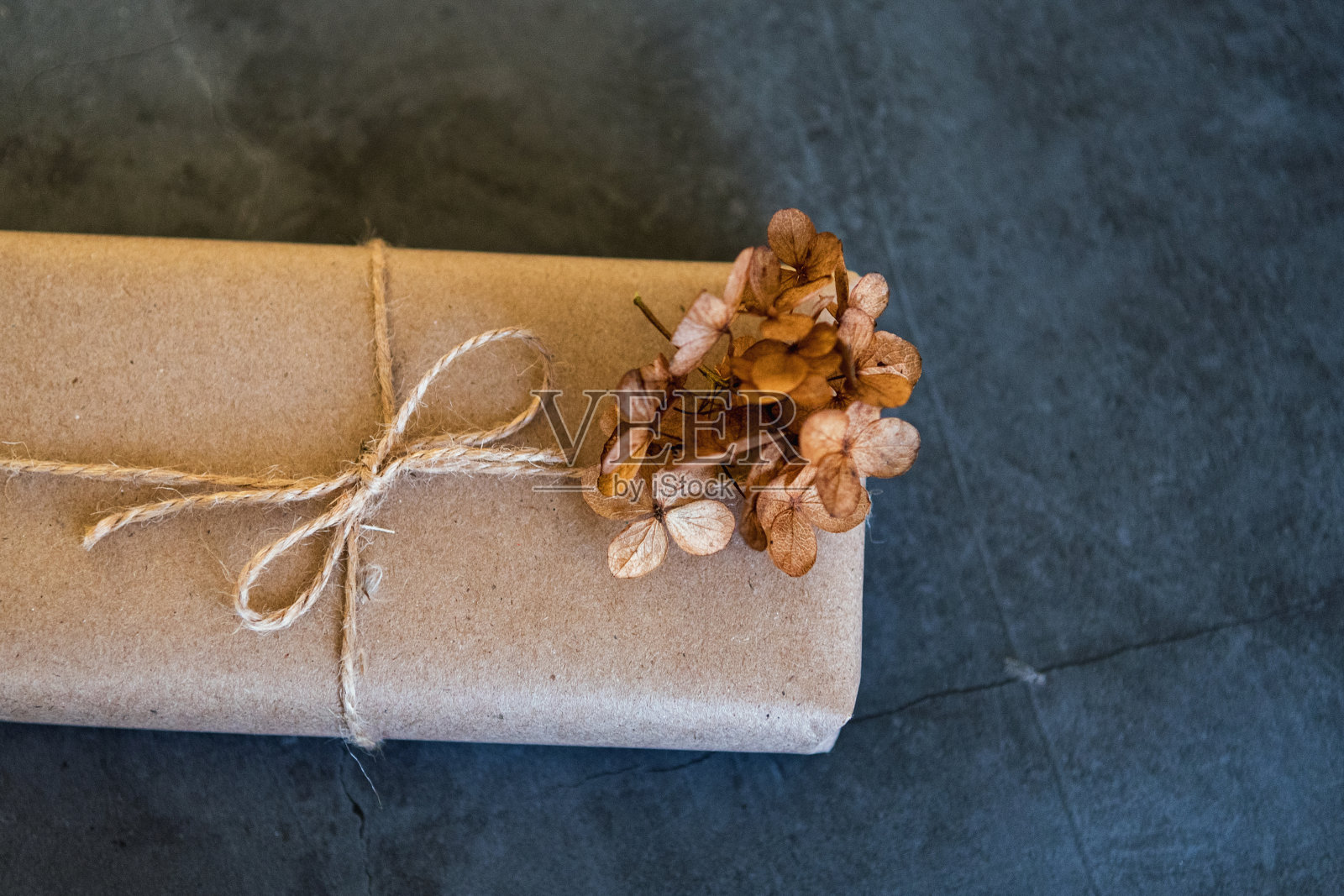 用牛皮纸包裹的礼盒,在黑暗的背景上有一个干绣球花。全新时尚装饰,拷贝空间。照片摄影图片