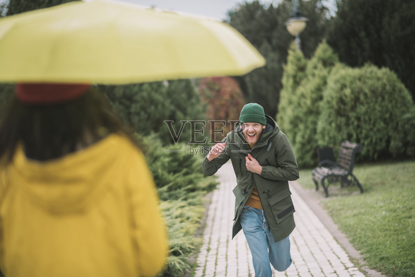 年轻男子跑向他的女朋友在黄色伞下照片摄影图片