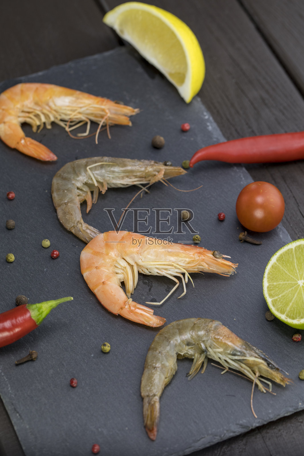 小虾放在石盘里,四周是黑多香果和酸橙照片摄影图片