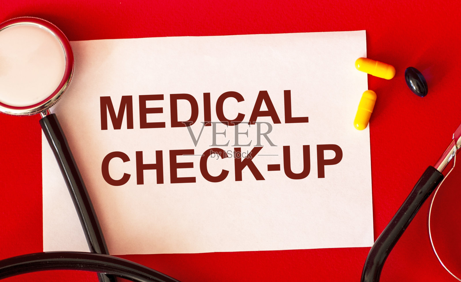 在一张白色的纸和红色的背景上写着“医疗控制”,旁边是听诊器和药片。医学和保健的概念。照片摄影图片