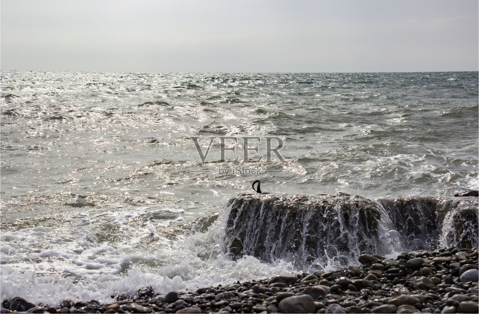 波涛汹涌的海面。灰蓝色,多云。泡沫拍打着海岸、岩石和防波堤。多云的天气。阳光反射在水中,闪烁不定。照片摄影图片