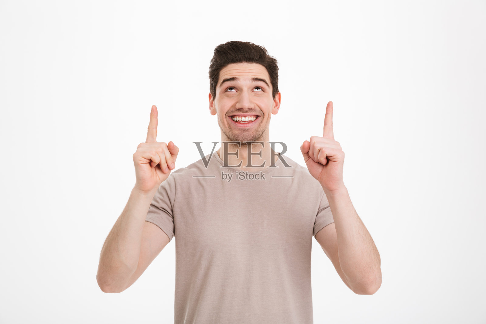 积极的褐发男子30岁,穿着米色t恤,手指向上的copyspace文本或产品,孤立在白色背景照片摄影图片