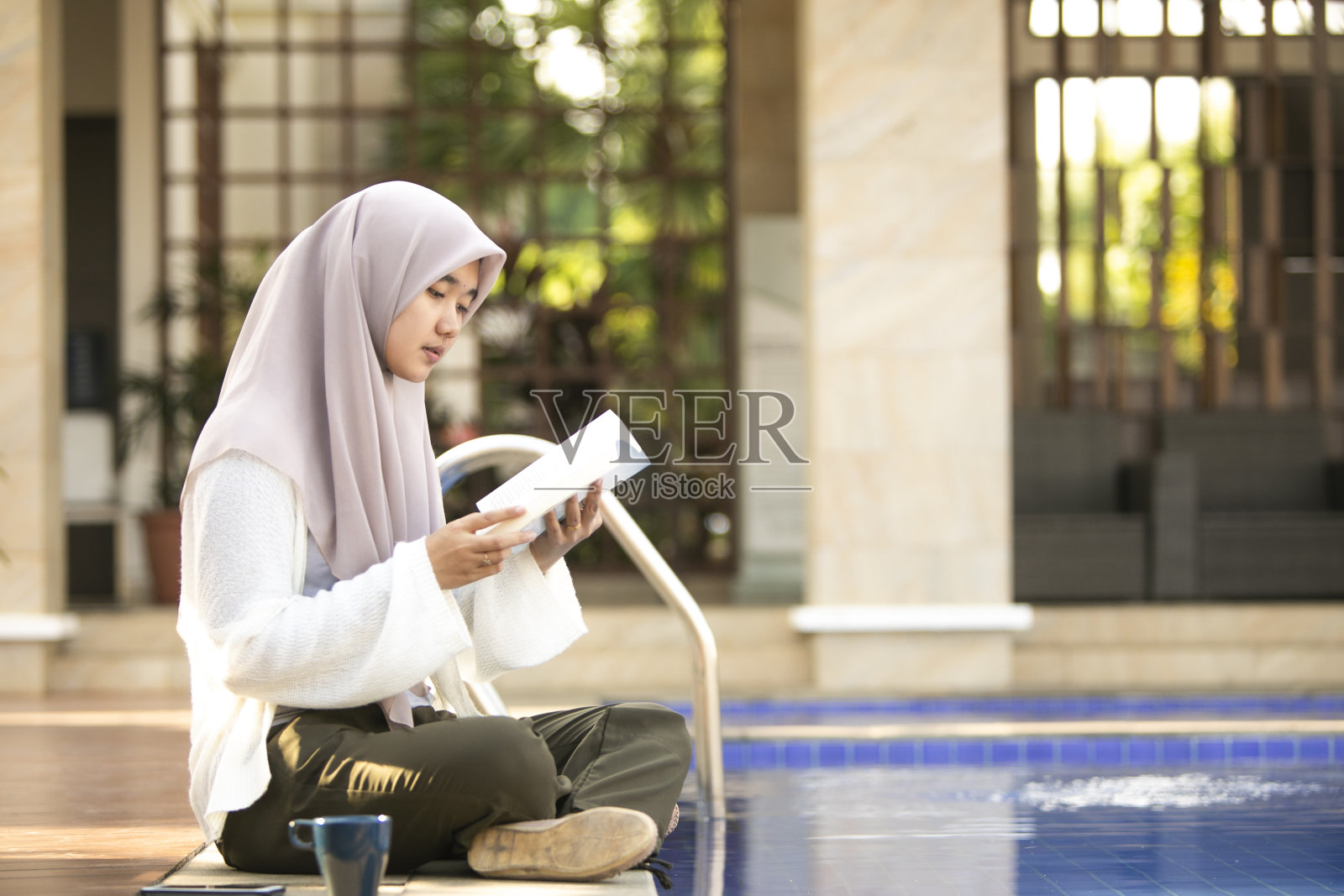 年轻的亚洲穆斯林妇女坐在泳池上读着书照片摄影图片