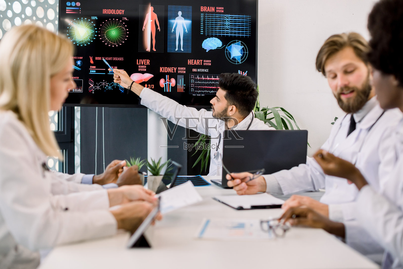 一位年轻的印度医生在一次医学会议上向他的多种族同事们建议,他指着一个大数字屏幕,上面有关于疾病症状和传播的信息和图片照片摄影图片