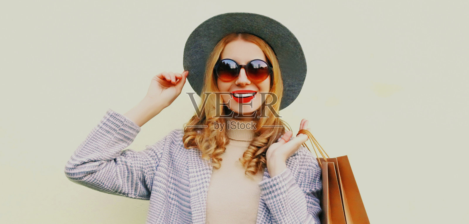 肖像时尚的金发女人与两个购物袋穿着外套,灰色圆帽的背景照片摄影图片