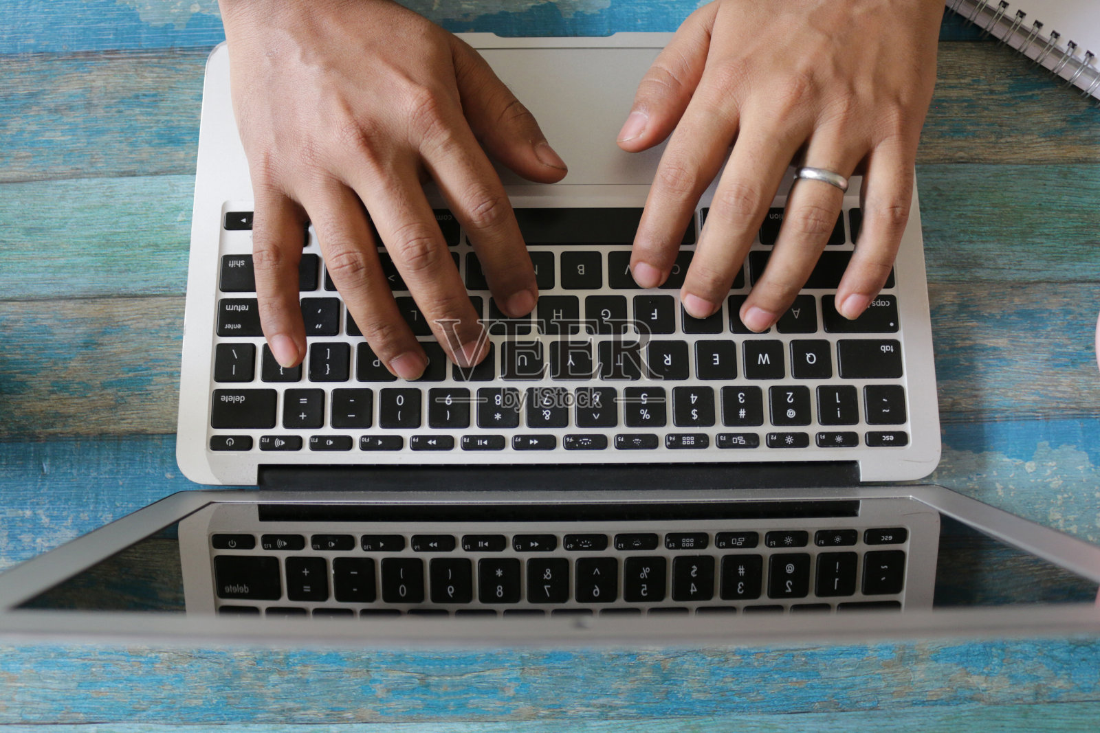 一个无法辨认的人在办公室工作站的笔记本电脑上打字,蓝色的木纹背景,高架的视野照片摄影图片