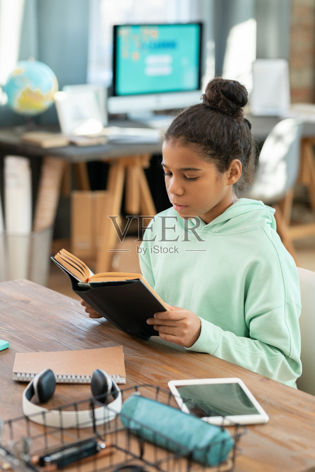 穿着休闲的可爱小学女生在客厅的桌旁看书照片摄影图片