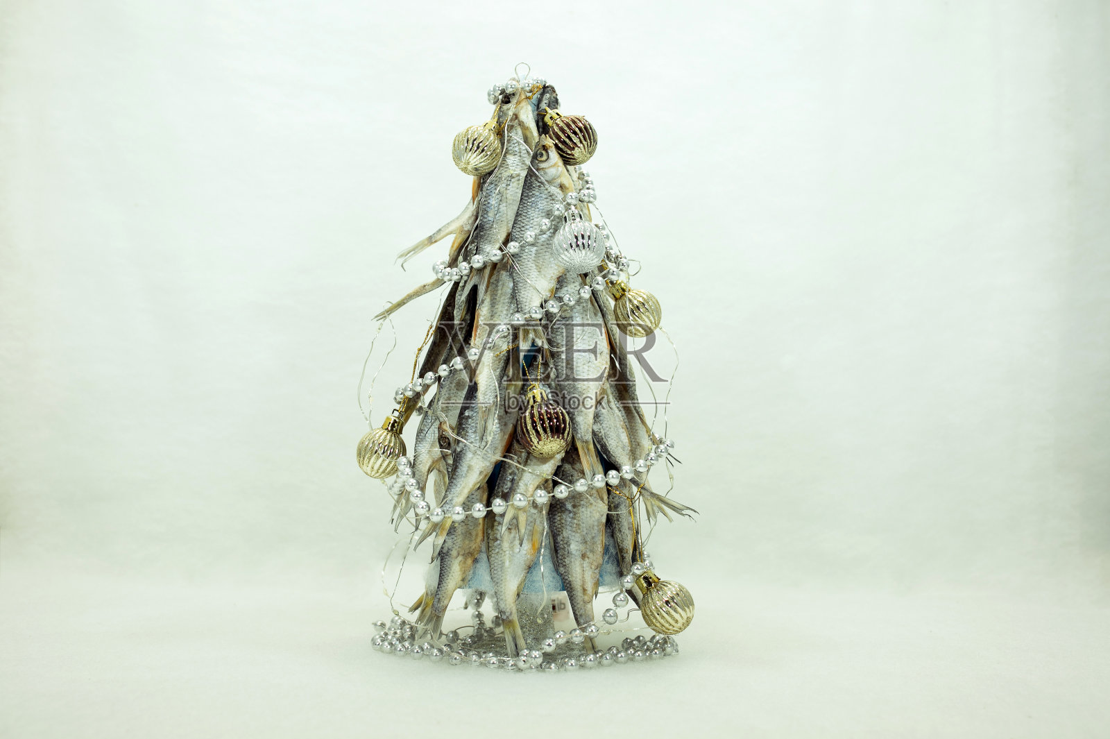 这棵圣诞树是用干鱼做的。圣诞树上装饰着新年的球和珠子。祝渔夫新年快乐。白色背景的特写。照片摄影图片