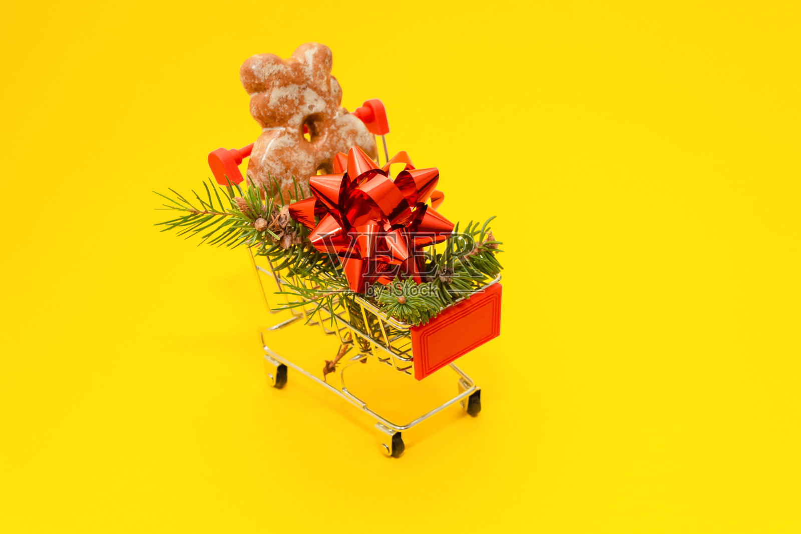 新年快乐。小购物车与冷杉树枝,礼品弓和姜熊在黄色的背景。节日装饰或明信片的概念。副本的空间。照片摄影图片