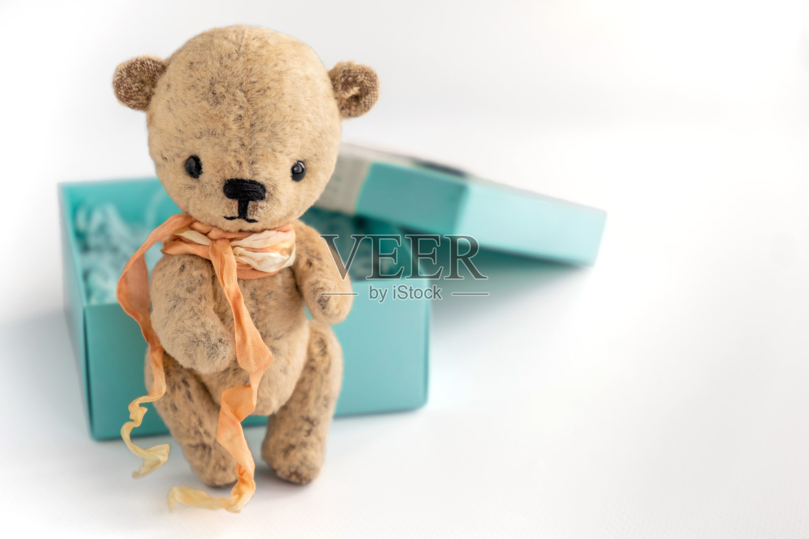 白色背景上,一个手工制作的小泰迪熊旁边是一个礼品盒。有选择性的重点。副本的空间。近距离照片摄影图片