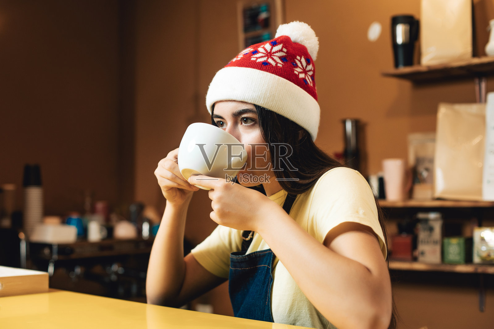 在咖啡店戴着圣诞帽做咖啡师的年轻女子。新年心情同一杯饮料。女孩正在喝咖啡照片摄影图片