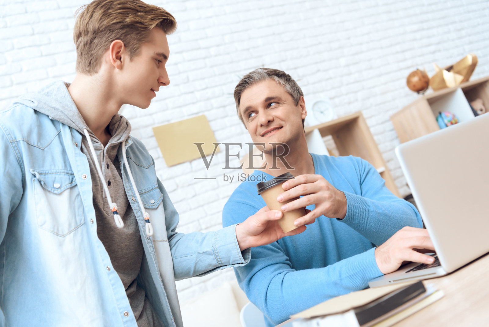 父亲在用笔记本电脑工作,儿子给他送来新鲜咖啡,制造惊喜。照片摄影图片