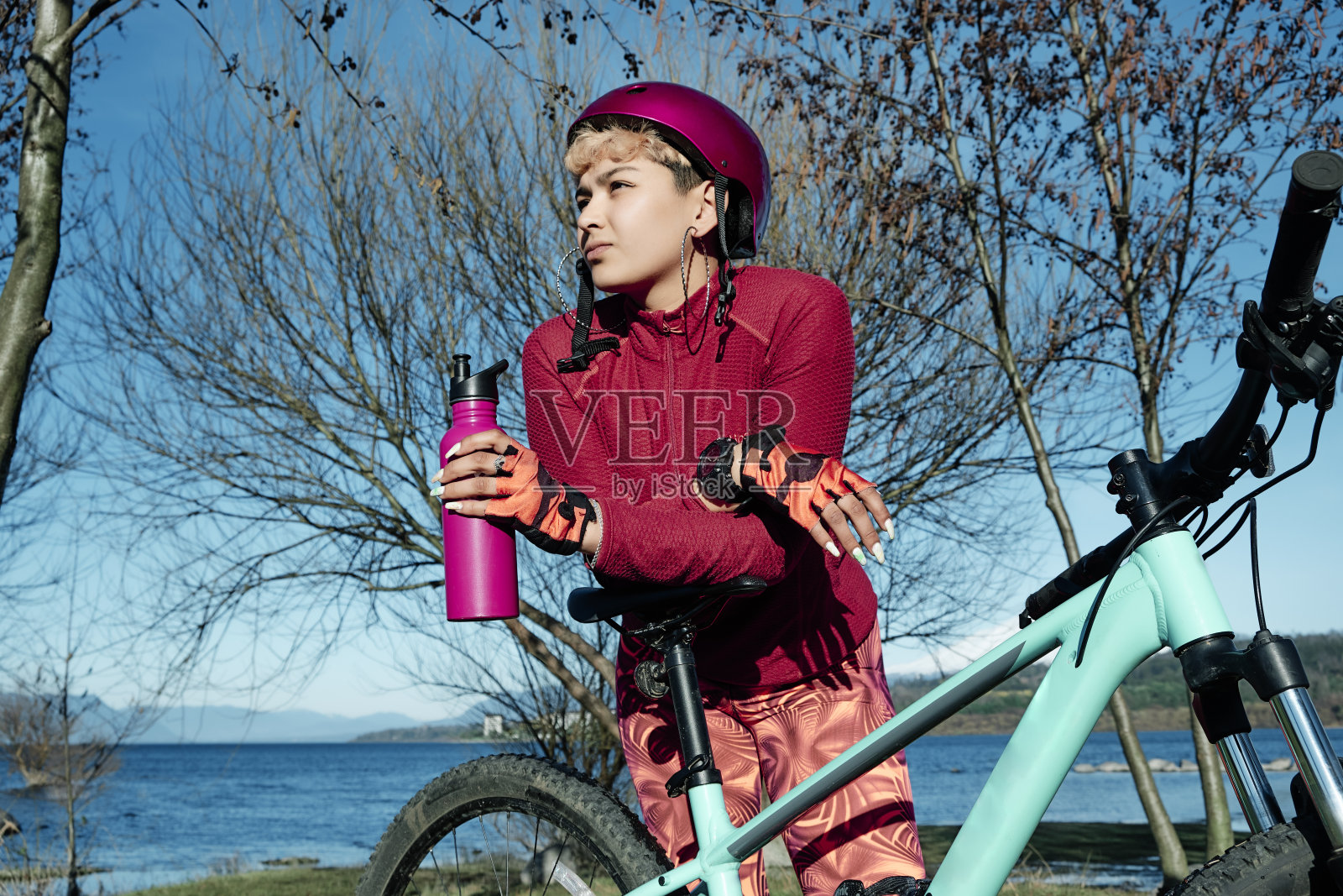 骑自行车的女孩在湖边等着,她的自行车上拿着一个运动瓶子照片摄影图片