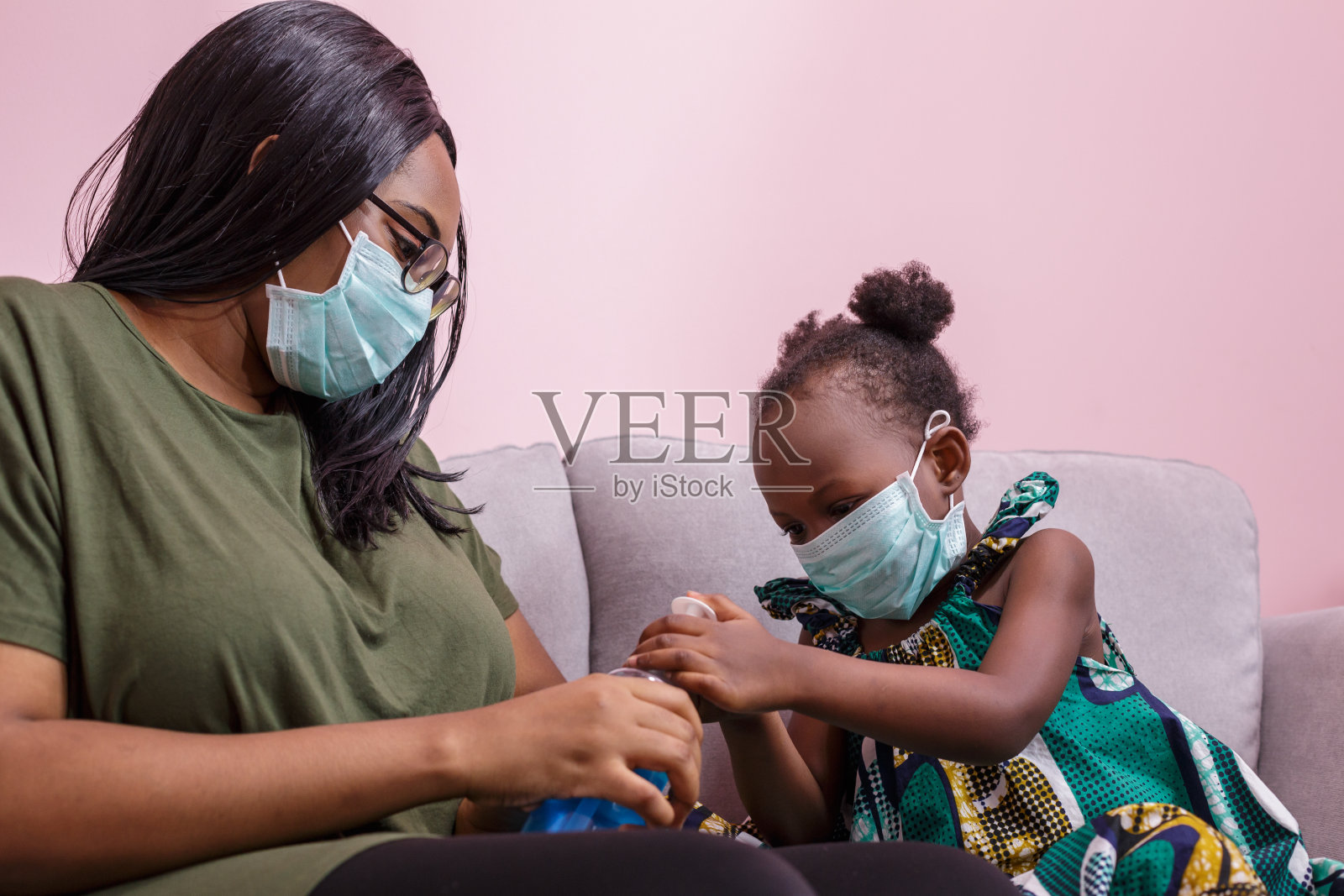 非洲裔美国人的母亲和女儿戴着口罩在家里用酒精洗手,以防止细菌和COVIC 19感染照片摄影图片