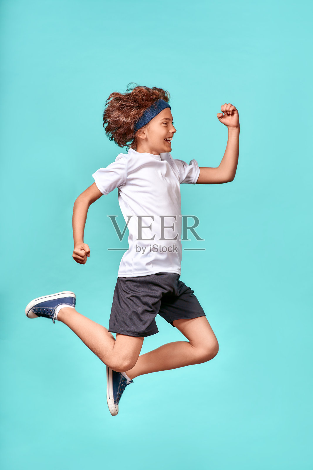 在运动。全长垂直镜头,一个快乐的,充满活力的青少年男孩跳跃在蓝色的背景孤立照片摄影图片