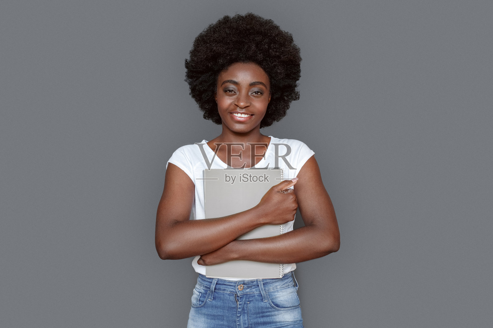 年轻女子孤立地站在灰色的拥抱杂志看着相机快乐照片摄影图片