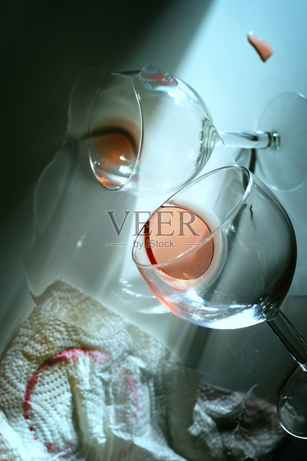 派对结束后,从一个不寻常的和令人困惑的角度,用两个掉在地上的玻璃杯,剩下的红酒和一个脏纸巾在条纹光,酒精上瘾的概念照片摄影图片