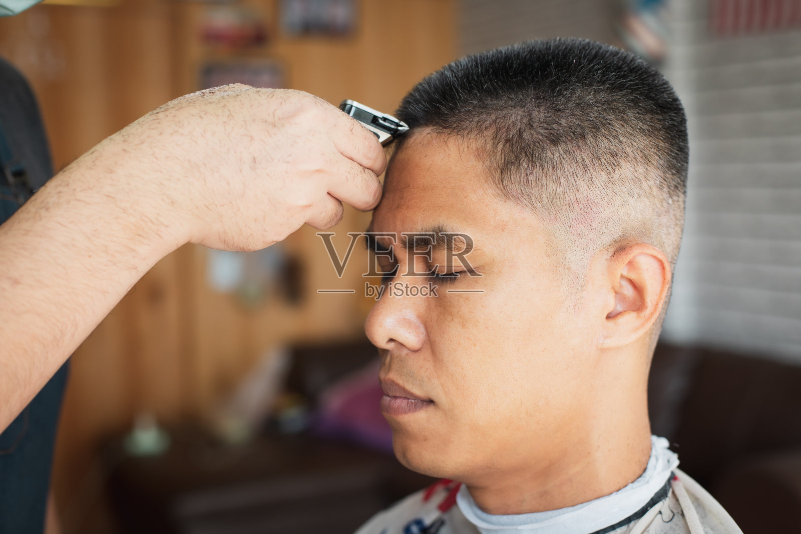 在理发店用电动剪子机理灰白头发的亚洲年轻人。照片摄影图片