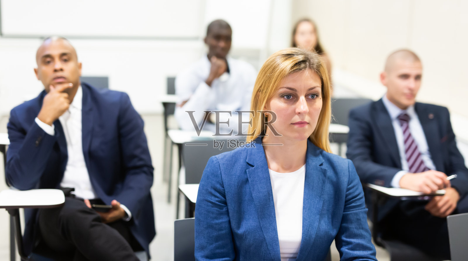 一名细心的女士被在会议室听演讲的同事包围着照片摄影图片