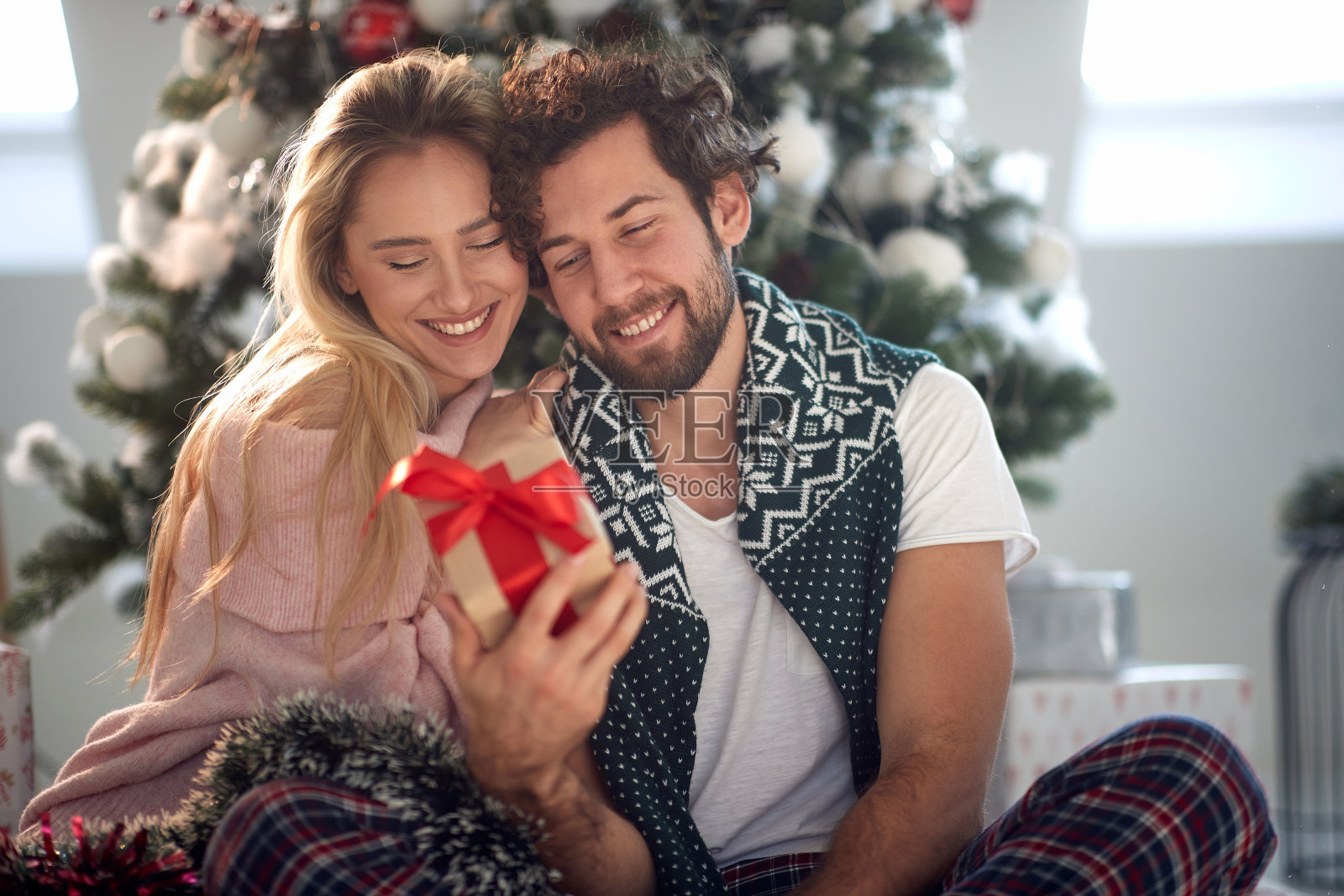 大胡子的家伙微笑着看着包裹在手里的礼物,漂亮的金发女郎靠在他的肩膀上照片摄影图片