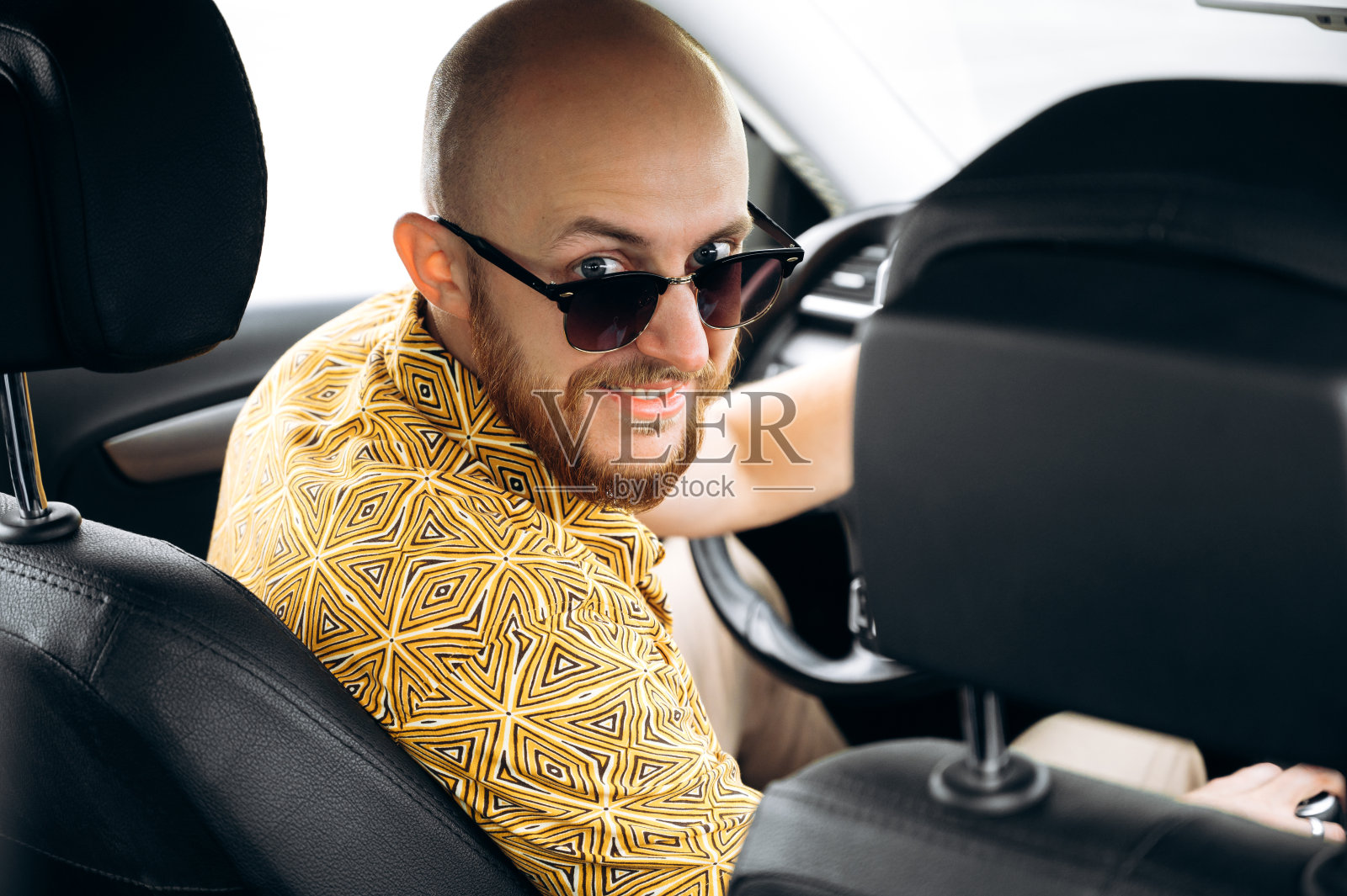 微笑的男子司机穿着时尚休闲装,戴着太阳镜坐在他的车的方向盘上看着镜头和微笑照片摄影图片