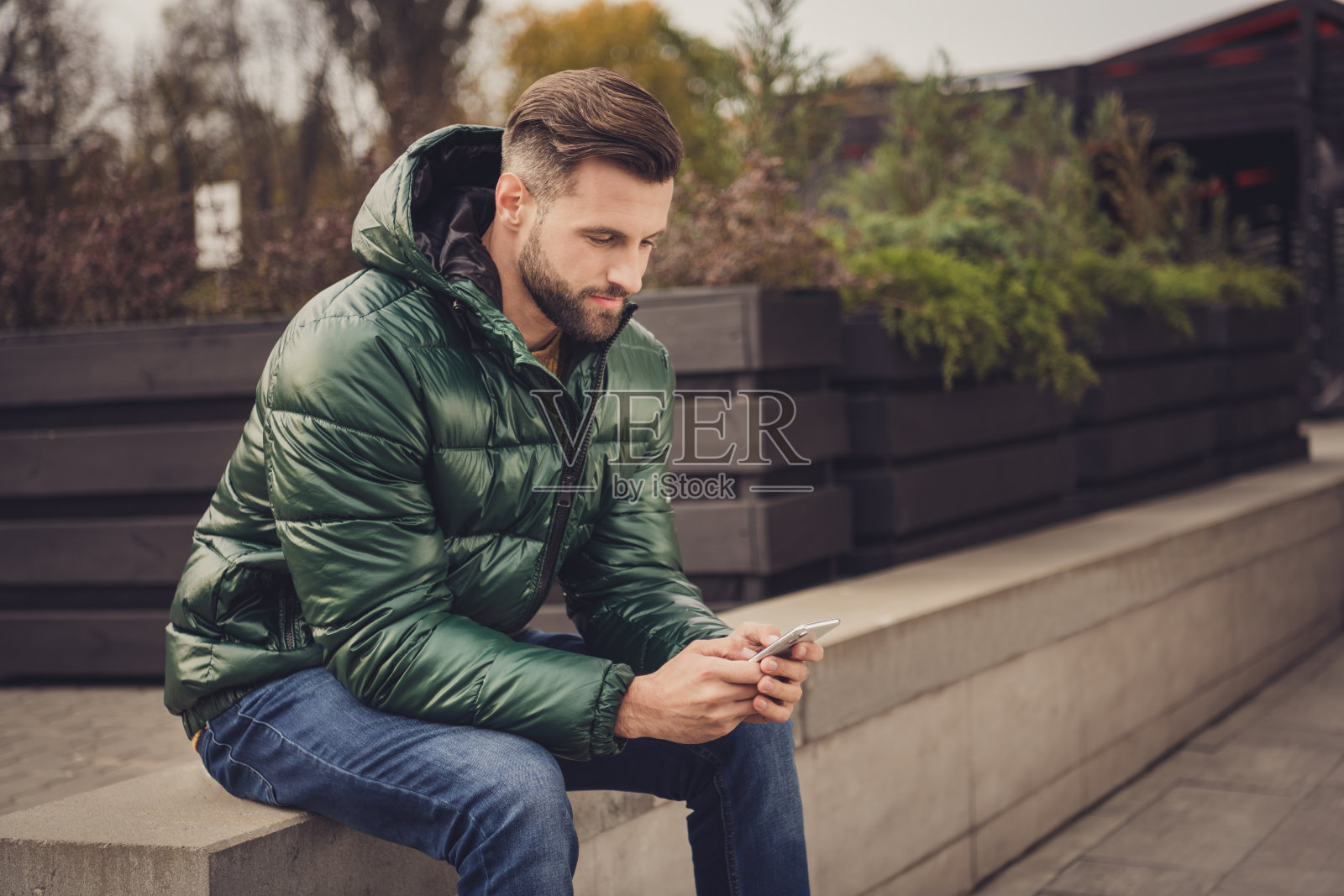 侧面照片英俊迷人的年轻男子穿着绿色风衣打字现代设备城外城市街道照片摄影图片