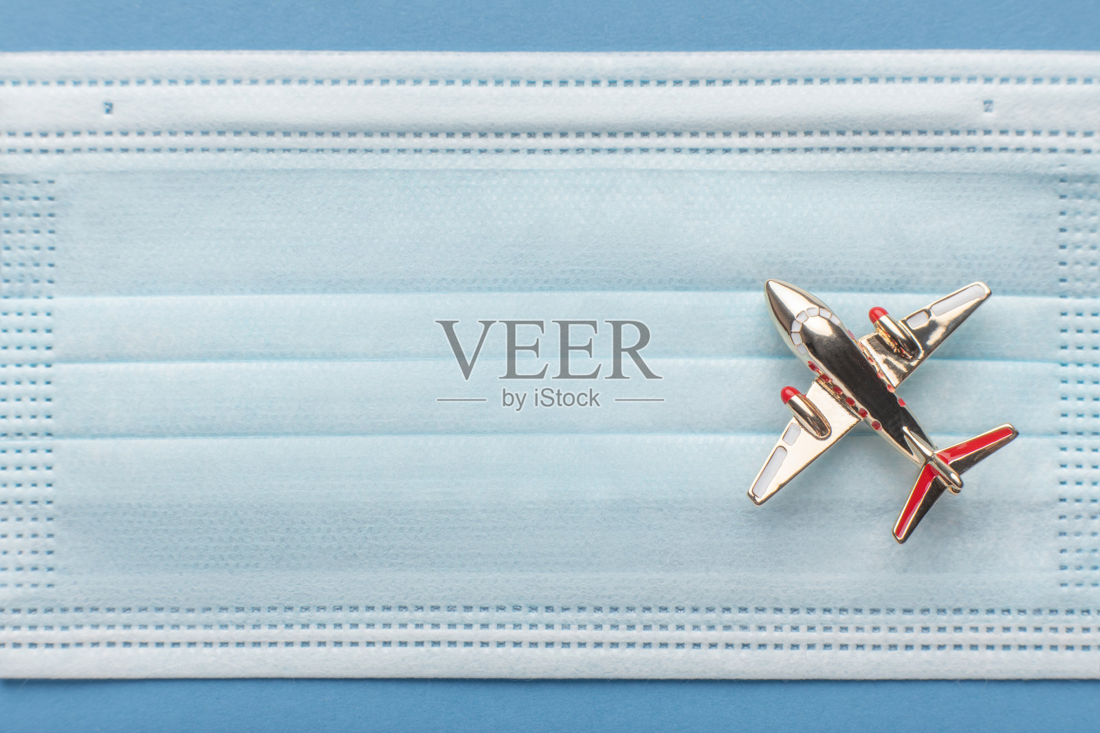 金色玩具飞机上方背景为冠状病毒药面罩。旅行限制和安全条例的概念。照片摄影图片