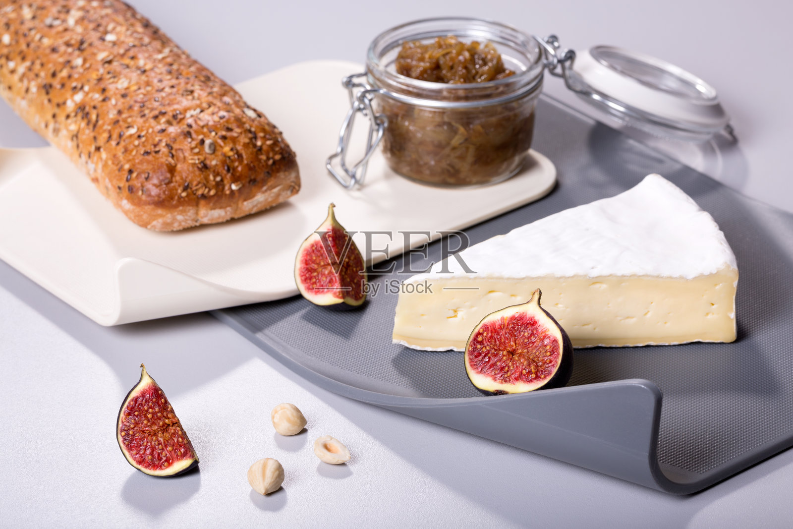 无花果配面包、洋葱果酱、布里干酪和榛子放在现代的塑料切菜板上。照片摄影图片