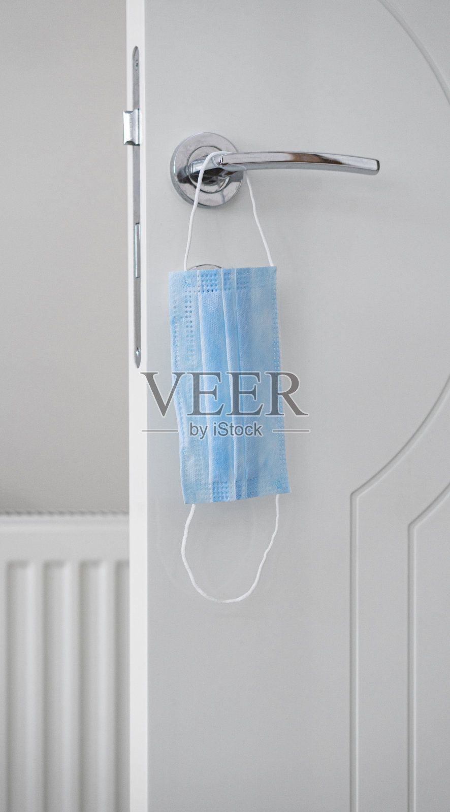 一个面具挂在一个公司大楼的门把手上,特写。提醒大家预防新冠肺炎大流行感染的安全措施照片摄影图片