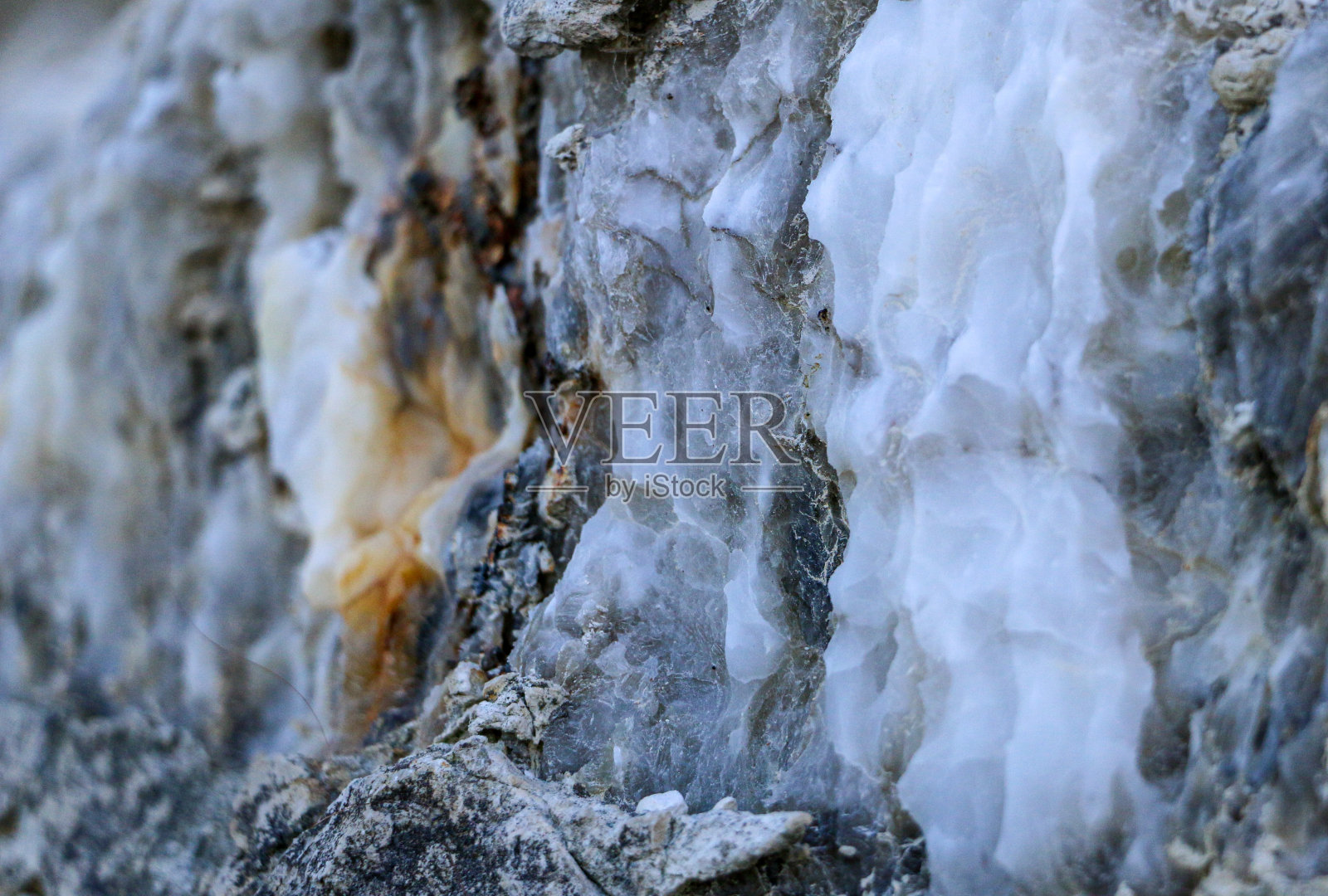 不同颜色的石英岩石在地球的切割。灰色,白色,橙色石英沉积物。未经处理的半宝石,各种各样的冰凝石矿床和不同的岩石层。照片摄影图片