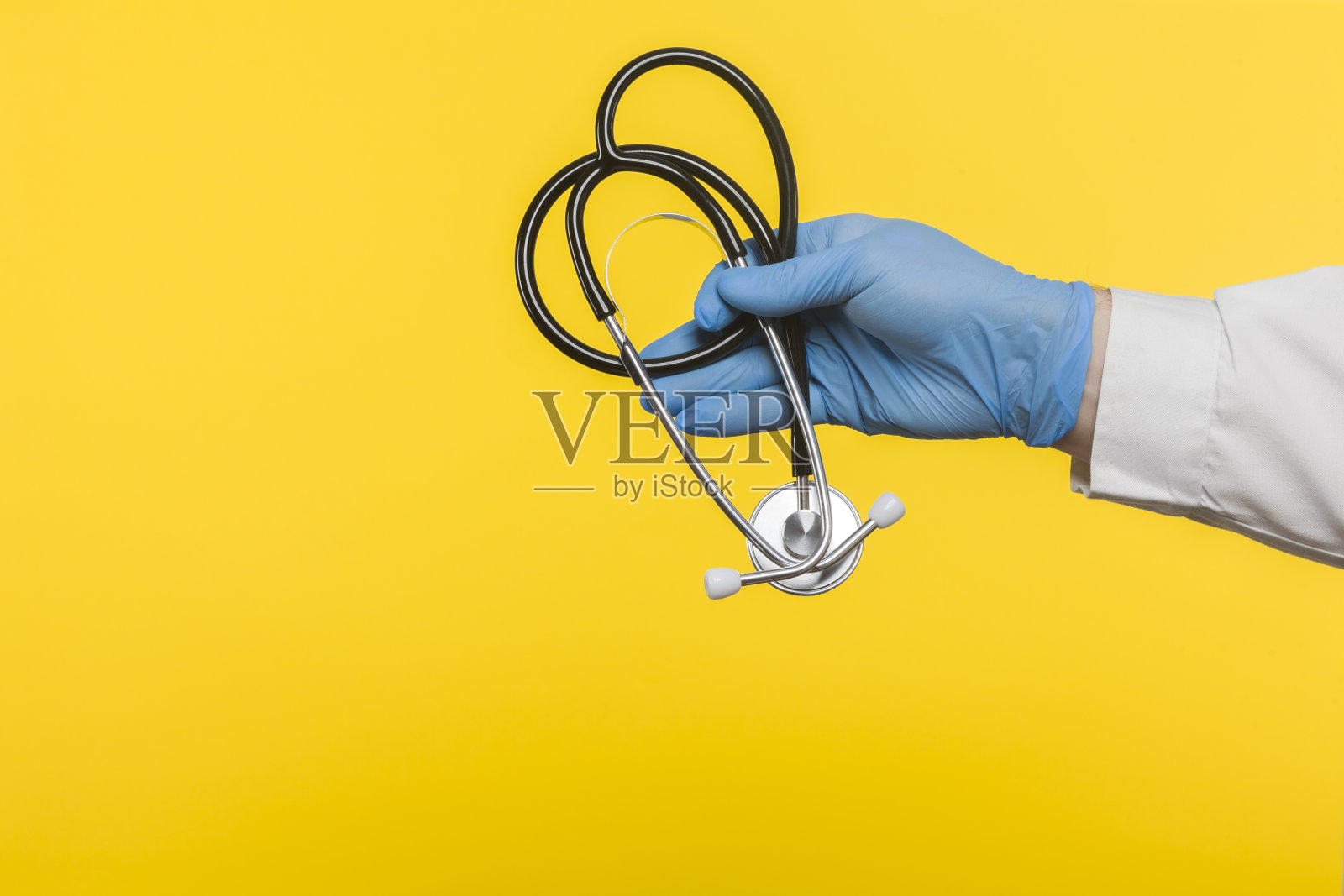 医生戴着防护手套,手持听诊器隔离在黄色背景上照片摄影图片