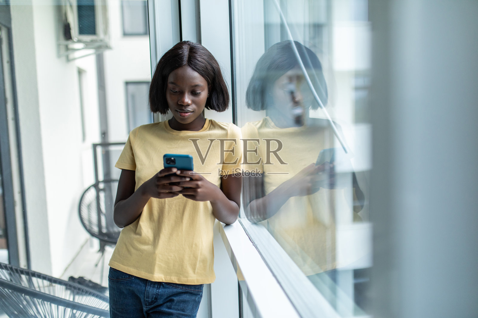 美丽的非裔美国妇女用手机看窗户坐在家里照片摄影图片
